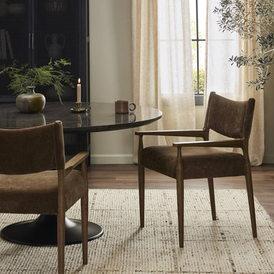 Luxury commercial hospitality dining room with a black marble round table, metal base, and brown wooden performance grade fabric chairs with arms near a window.