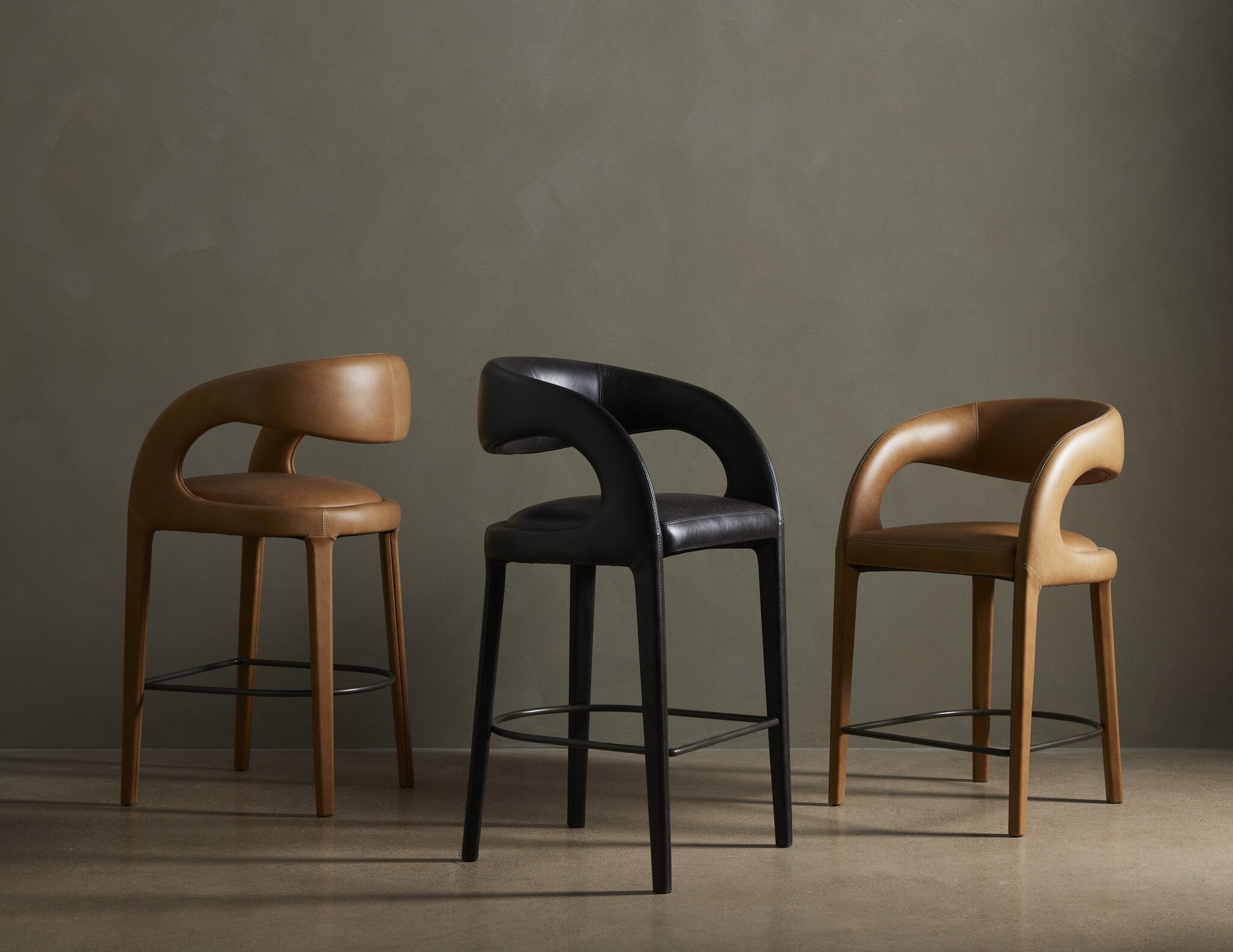 Set of counter stools with curved armrests, upholstered seats, and black metal footrests.