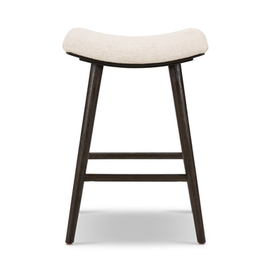 A bar stool with a light beige upholstered saddle-style seat and dark brown carbon-finished oak legs. Union Bar Stool in Essence Natural fabric with a light carbon-finished oak saddle-style seat.
