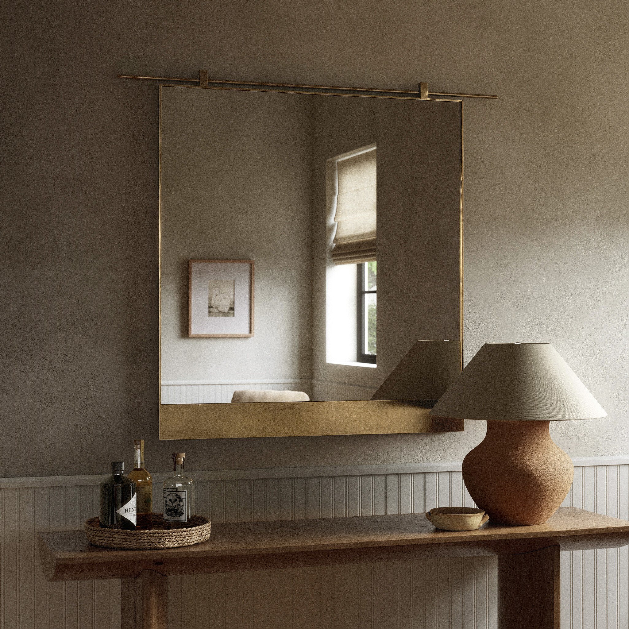 Chico small square wall mirror with a vertical antique brass suspension bar on a wall above a wooden console table with decorative items