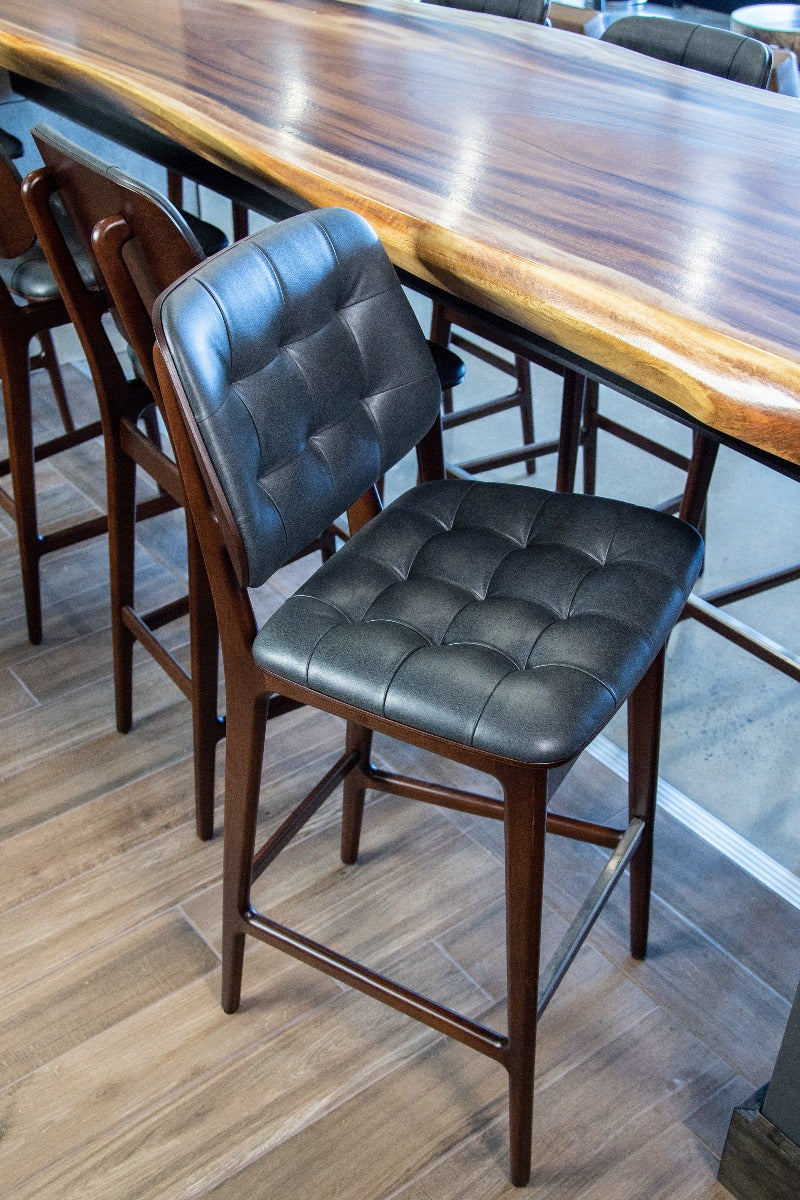 Tufted bar stool with blue cushioned seat, tufted back, and dark wood frame
