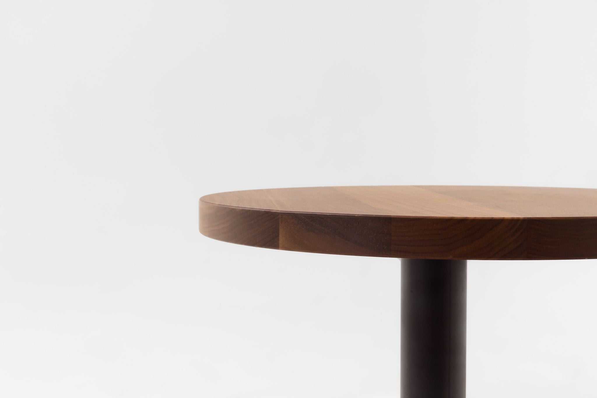 Dark-brown walnut table top edge with a smooth finish and black base post.